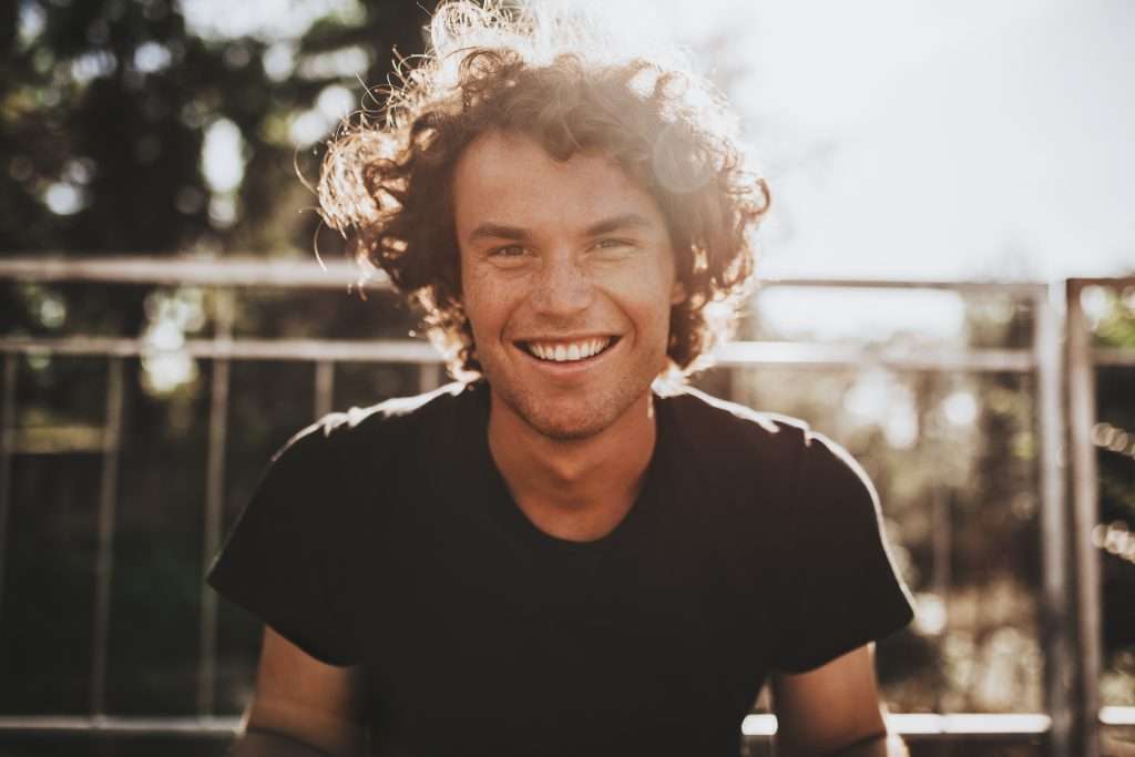 Outdoor closeup of a handsome smiling man with curly hair in the city at sunset, representing Charlotte psychiatry services